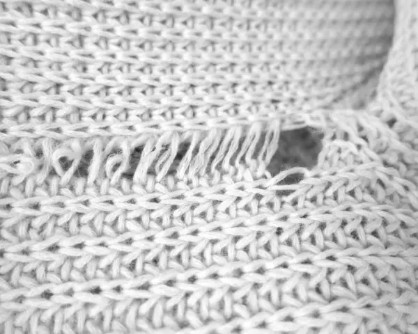 Nahaufnahme eines weißen Strickpullovers mit einem Loch und ausgefransten Fäden. Was tun, wenn die Wolle eingelaufen ist?