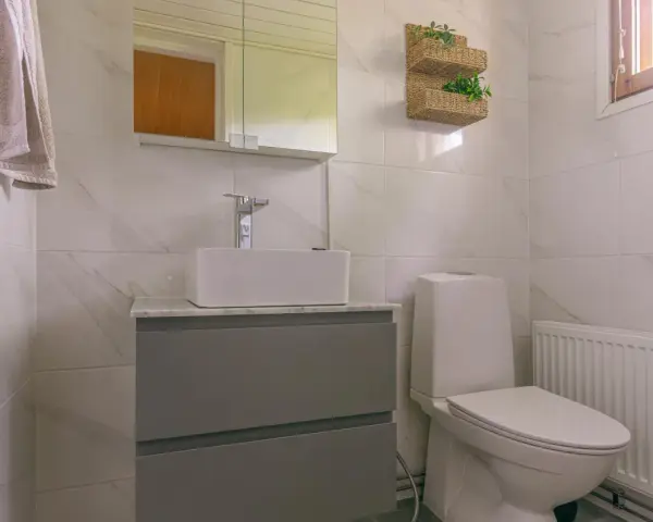 Modernt badrum med handfat och toalett utan avlopp. En handduk hänger på väggen.