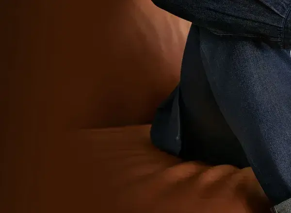 Uomo con jeans scuri seduto su divano in pelle. Scopri come lavare jeans a mano per mantenerli perfetti.