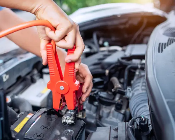 Hands connect jumper cables to a car battery, a common fix when wondering how long can a car be on before the battery dies.