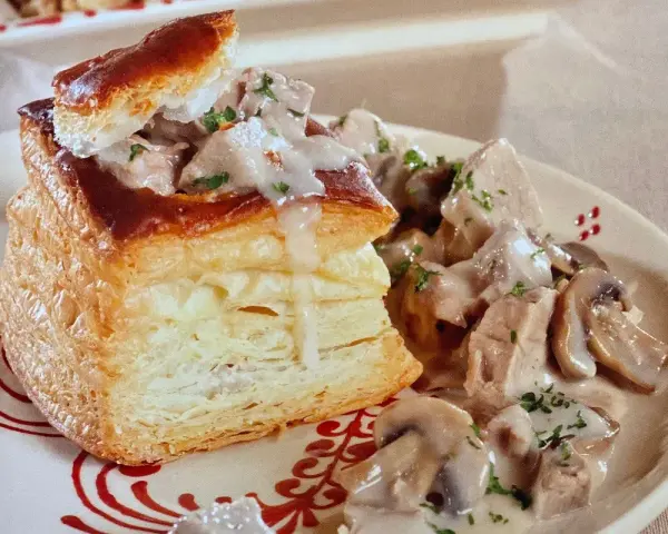 Une bouchée à la reine au veau, garnie de morceaux de veau et de champignons dans une sauce crémeuse, servie sur une assiette décorée.