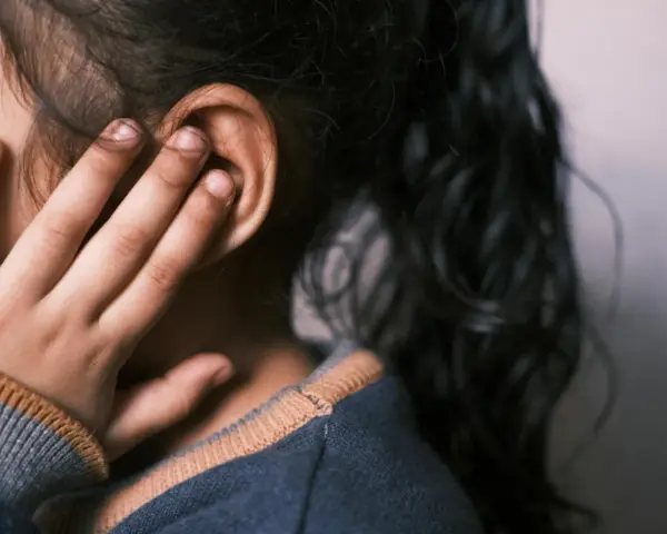 Dziecko z domowymi sposobami na ucho pływaka. Dłoń zasłania ucho, włosy opadają na twarz.
