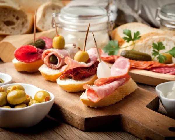 Pyszne tapas na drewnianej desce: pieczywo z wędliną, oliwkami, ogórkiem i suszonymi pomidorami.
