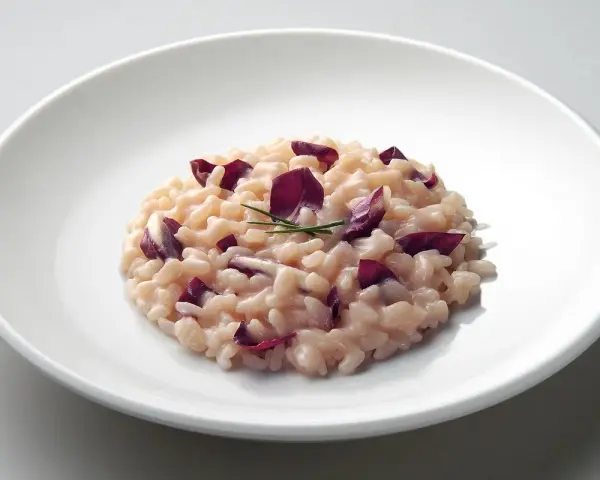 Un cremoso risotto al radicchio rosso, guarnito con erba cipollina, servito su un piatto bianco.