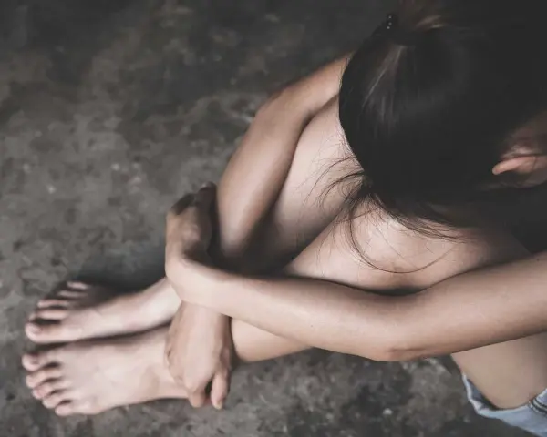 En person sitter hopkrupen på ett betonggolv, med armarna runt knäna. Bilden kan symbolisera depression och dess fysiska symptom.