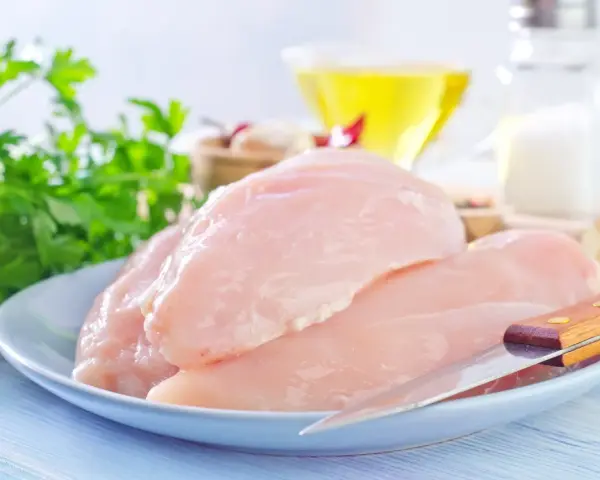 Surowe filety z kurczaka na talerzu, gotowe do przygotowania. W tle olej, sól i natka pietruszki. Idealne dla dbających o filet z kurczaka kcal.