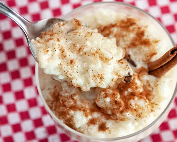 Cuchara con cremoso arroz con leche, espolvoreado con canela. ¿Quién inventó el arroz con leche? ¡Este postre es un clásico!