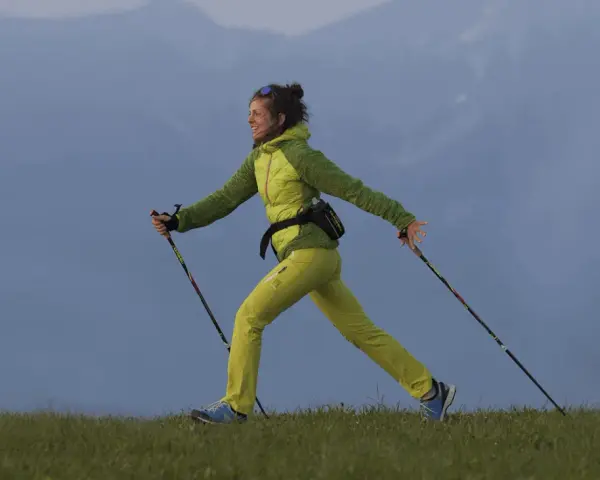Donna sorridente pratica nordic walking su un prato. Informarsi sulle controindicazioni prima di iniziare.