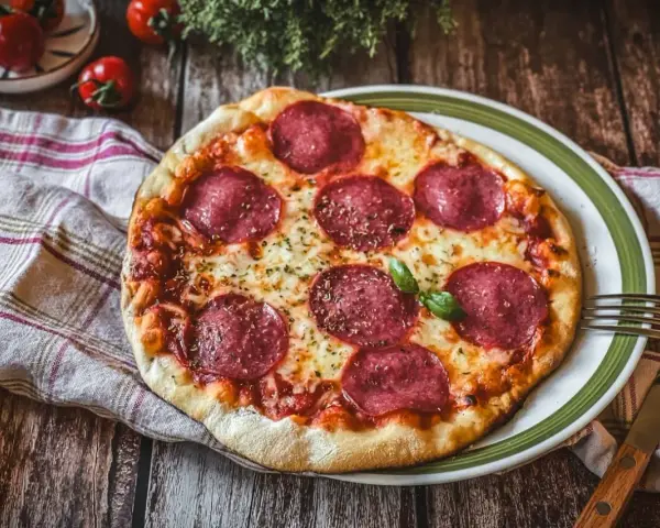 Eine köstliche Pizza Salami mit geschmolzenem Käse und frischem Basilikum auf einem rustikalen Holztisch.