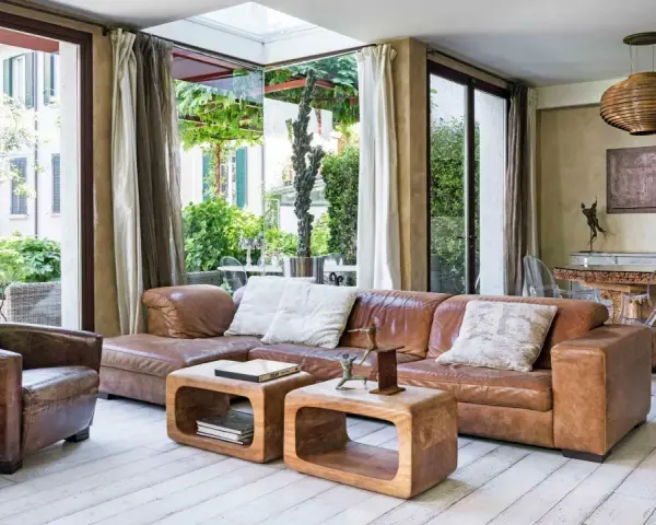 Accogliente soggiorno etnico chic con divano in pelle, poltrona vintage e vista sul verde.