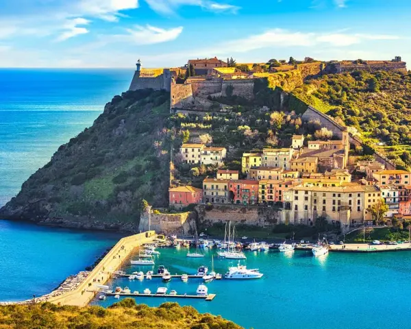 Incantevoli toscana paesaggi: un borgo colorato su una collina fortificata domina un porto con barche, baciato dal sole.
