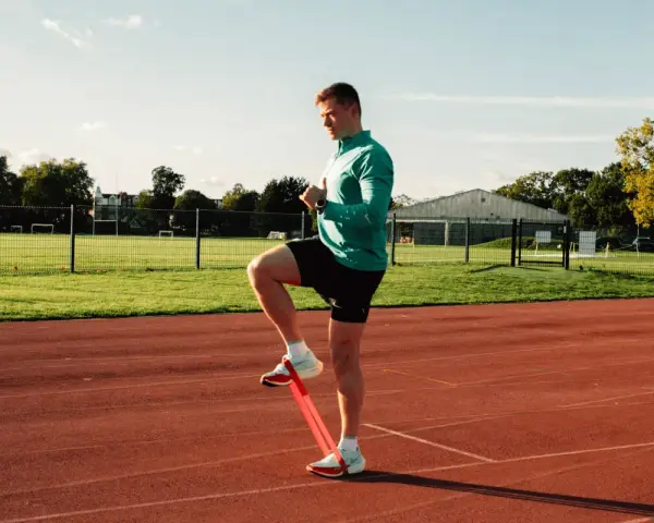 Uomo si allena con elastico sulle caviglie in pista, pronto a riprendere a correre.
