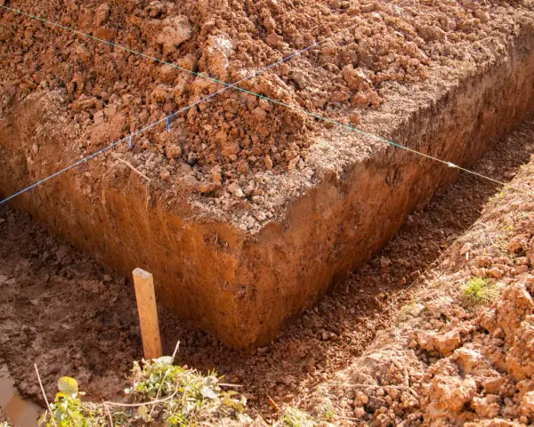 Wykonano wykop pod ławy fundamentowe. Widać ziemię, sznurki wyznaczające linie i drewniany palik.