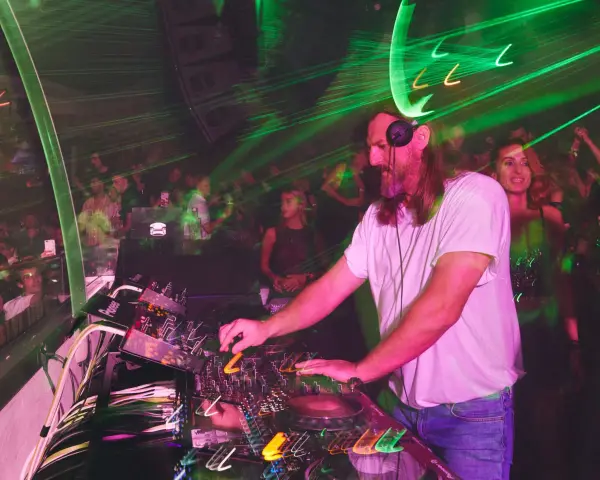 DJ w białej koszulce grający na konsoli w klubie z zielonymi laserami.