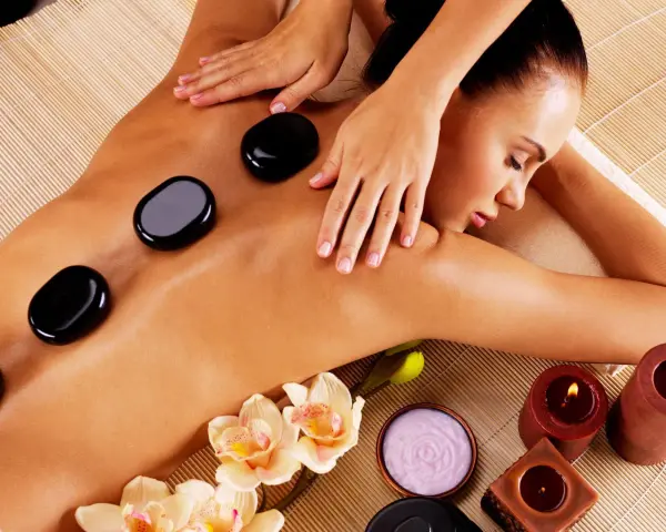 A woman enjoys the benefits of hot stone massage, with smooth black stones placed on her back. Orchids and candles add to the serene spa atmosphere.
