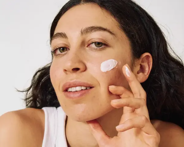 Frau mit zu Akne neigender Haut trägt eine leichte Creme auf.