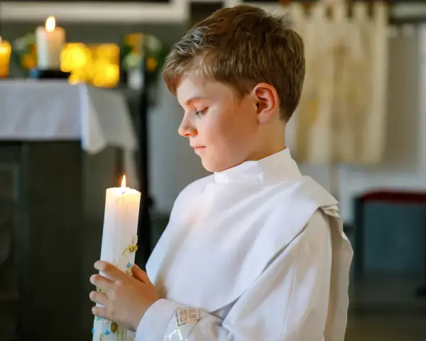 Chłopiec w bieli trzyma zapaloną świecę podczas uroczystości chrztu świętego.