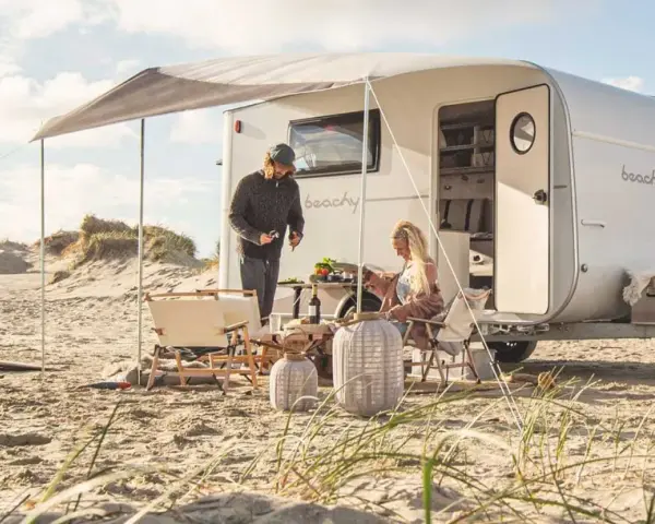 Ett par njuter av en stranddag med sina tyska husvagnar. Solen skiner och sanddynerna skapar en vacker bakgrund.