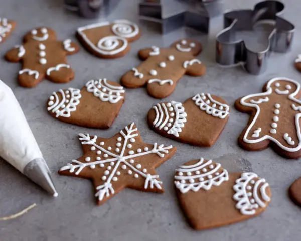 Pepparkakshus och hjärtan dekorerade med vit kristyr. En sprits med kristyr ligger bredvid.