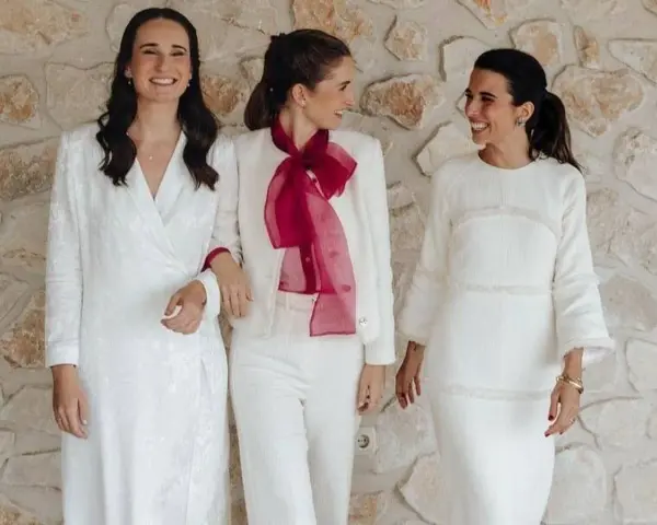 Tres mujeres sonríen vestidas de blanco, demostrando que se puede ir de blanco a un bautizo.