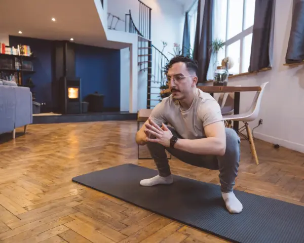 Homme en tenue de sport effectuant un étirement pubalgie sur un tapis de yoga dans un salon moderne.