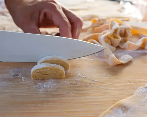 Hand schneidet frisch zubereitete, selbstgemachte Pasta auf einem Holzbrett.