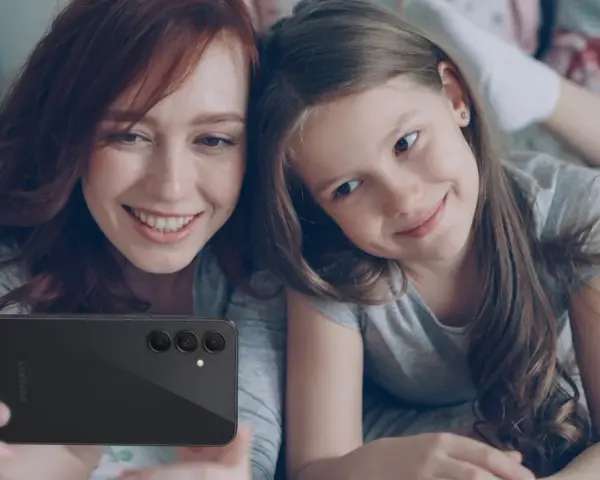 Mama i córka robią selfie telefonem. Od ilu lat można mieć telefon? Odpowiedź zależy od rodziców i dziecka.