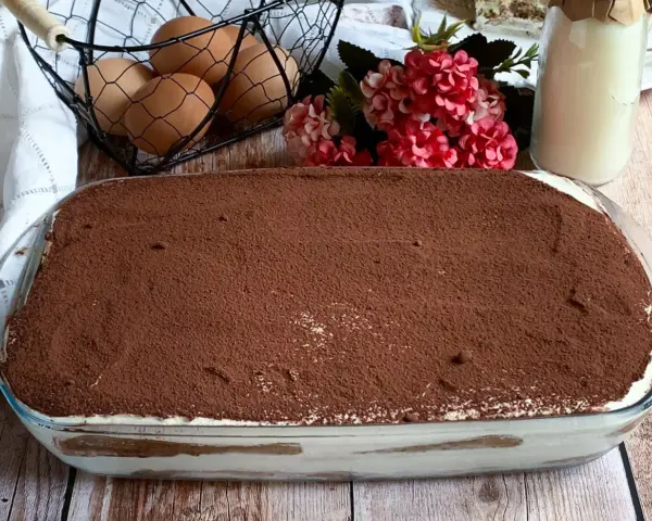 Tiramisù pronto, con 250 gr di mascarpone, pronto per essere gustato. Ingredienti freschi come uova e fiori decorano la tavola.