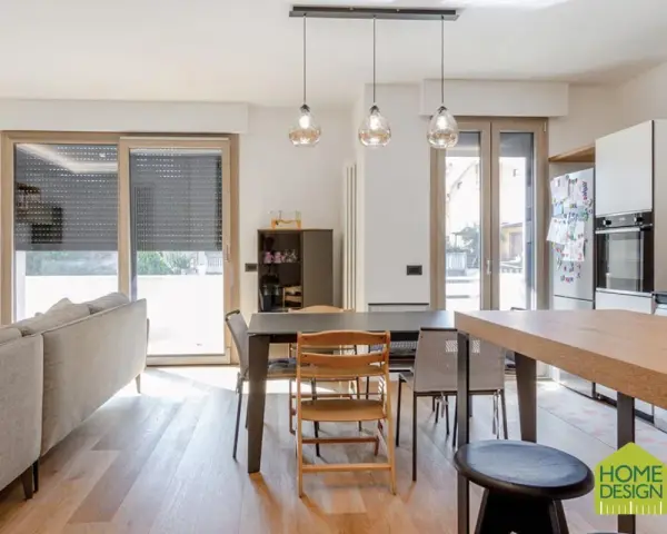Un soggiorno luminoso con un divano, tavolo da pranzo e cucina a vista. Un moderno sopraluce illumina l'ambiente.