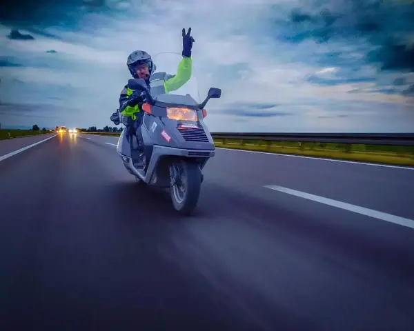 Karta motorowerowa w akcji! Kierowca w kasku i kamizelce odblaskowej pozdrawia, jadąc skuterem po autostradzie.