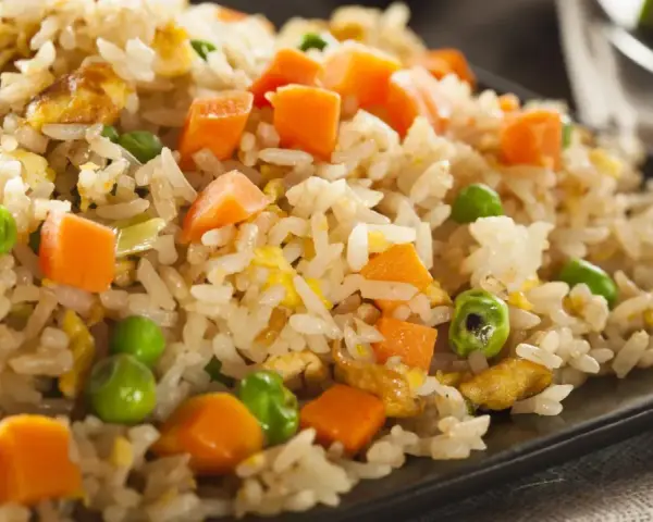 Arroz tres delicias con guisantes y zanahoria en un plato negro.