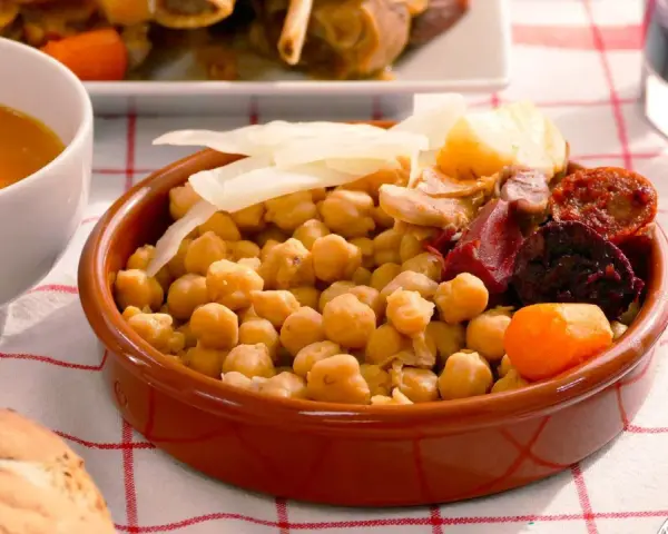 Cocido madrileño con garbanzos, chorizo, morcilla, patata y zanahoria en cuenco de barro.