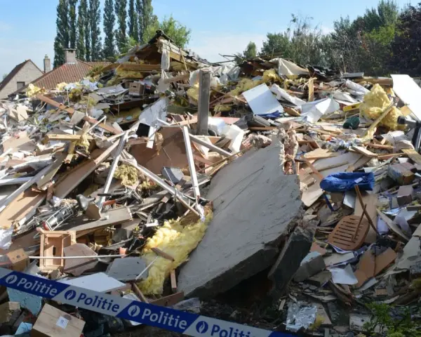 Ogromna kupa gruzów po zawaleniu się budynku. Widać izolację, drewno, beton i niebieską torbę. Wstęga policyjna zabezpiecza teren.