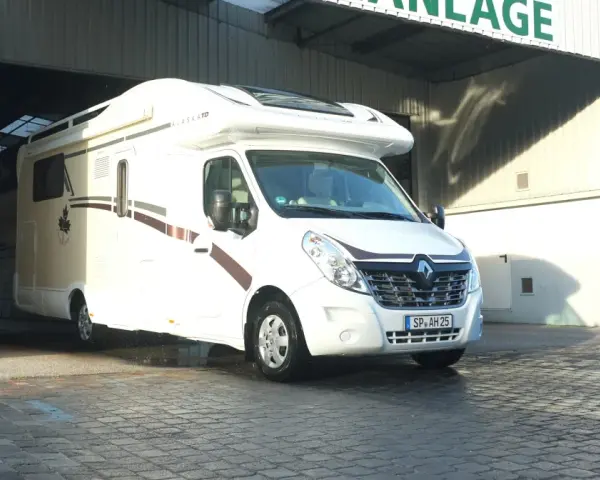 Biały kamper Alaska TD wyjeżdża z zadaszonego miejsca, gotowy na przygodę. Idealny na rodzinny camper park.