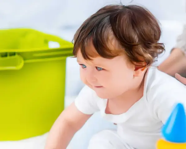 Mały poszukiwacz sensoryczny z zaciekawieniem odkrywa świat, obok niego zielony pojemnik i kolorowe zabawki.