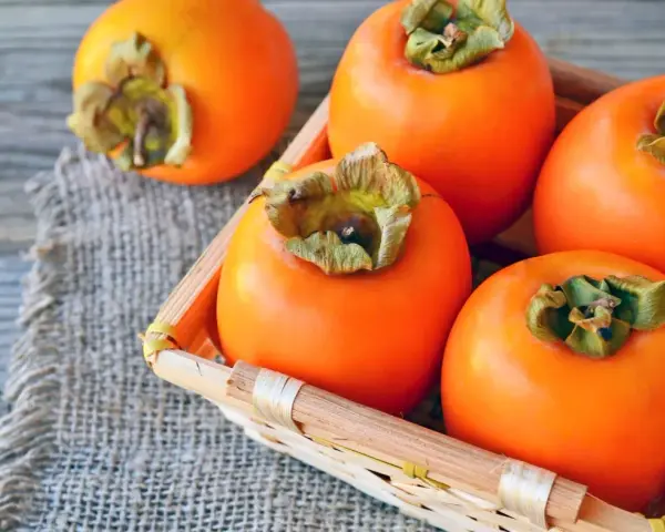 Frische, orangefarbene Kaki-Früchte liegen in einem kleinen Korb auf grobem Leinen. Kaki gesund und lecker.