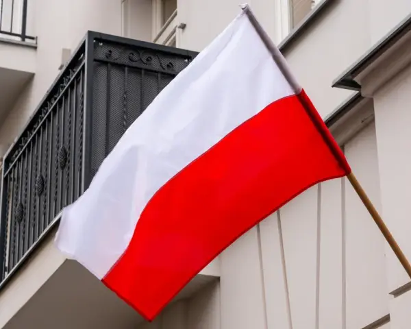 Flaga Polski w pionie, biało-czerwona, powiewa na tle budynku z balkonem.