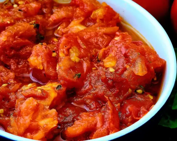 Un tazón de tomates picados, jugosos y vibrantes, con un toque de albahaca fresca y dos tomates enteros al fondo. Un bonito con tomate listo para disfrutar.