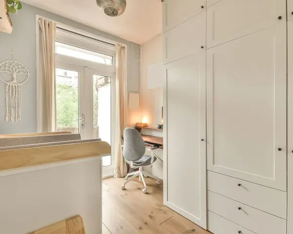 Un angolo studio in camera da letto, con scrivania, sedia girevole e armadio bianco.
