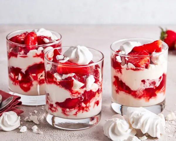 Drei Gläser mit Eton Mess: geschichtete Erdbeeren, Sahne und zerbrochene Baiser-Stücke.