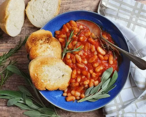 Fagioli all'uccelletto in umido con pomodoro, serviti con pane tostato e erbe aromatiche. Perfetti per scoprire cosa abbinare ai fagioli all'uccelletto.