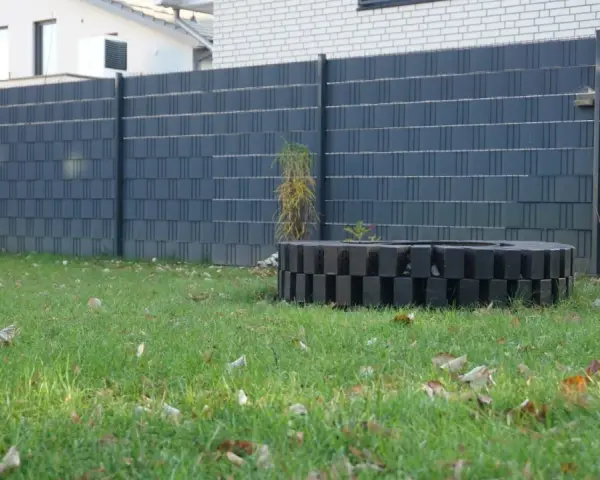 Moderner Sichtschutzzaun, der sich gut zum zaun selber bauen billig eignet. Ein dekorativer Kreis aus schwarzen Steinen im Garten.
