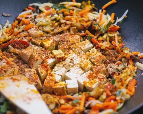 Kawałki tofu i kolorowe warzywa po chińsku smażą się na patelni wok, przyprawione kurkumą i papryką.
