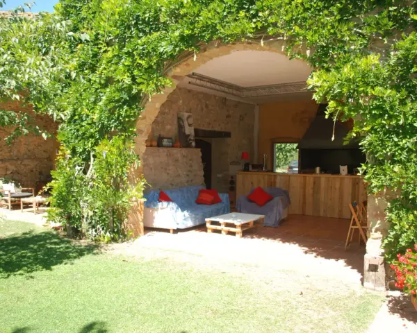 Un jardín con una madreselva planta cubriendo un arco de piedra. Dentro, sofás y una barra de madera.