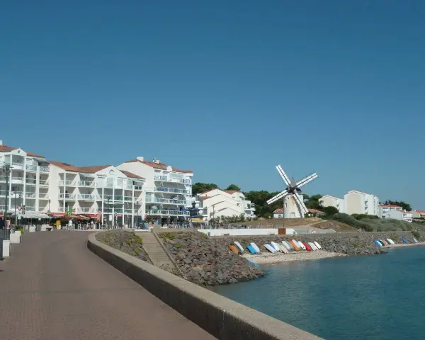 Vue de Jard-sur-Mer avec son port, ses immeubles blancs, son moulin et sa plage bordée de bateaux.