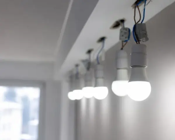 Rząd białych żarówek LED, wiszących na przewodach, świeci jasno, mimo że instalacja wygląda na nieukończoną.