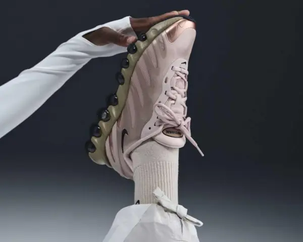 Różowy but Nike na obcasie, trzymany przez dłoń w białej rękawiczce.