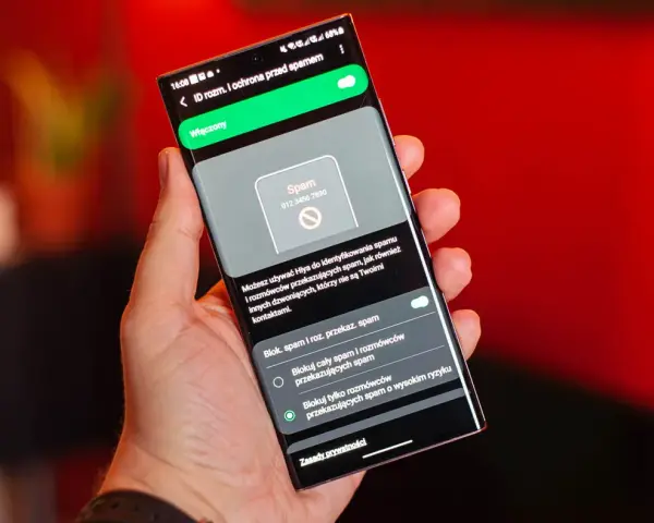 Dłoń trzyma smartfon z włączoną ochroną przed spamem. Ekran pokazuje powiadomienie o potencjalnym spamerze, gdy dzwonią z laboratorium.