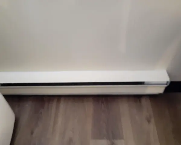 Dylatacja posadzki przy ścianie, biała listwa przypodłogowa z czarną szczeliną, drewniana podłoga.
