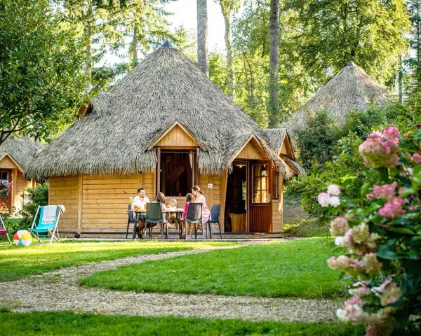 Famille profitant d'un repas en terrasse devant leur chalet en chaume, parfait pour des vacances scolaires en Bretagne.